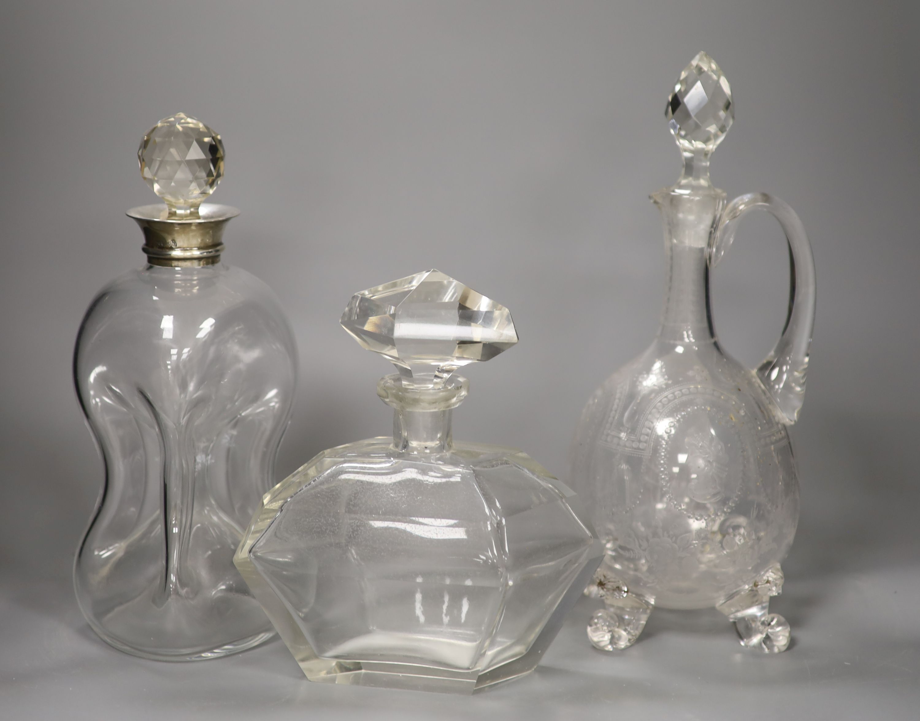 A George V silver collared decanter, a facet cut glass decanter and a wheel engraved glass claret jug with associated stopper, tallest